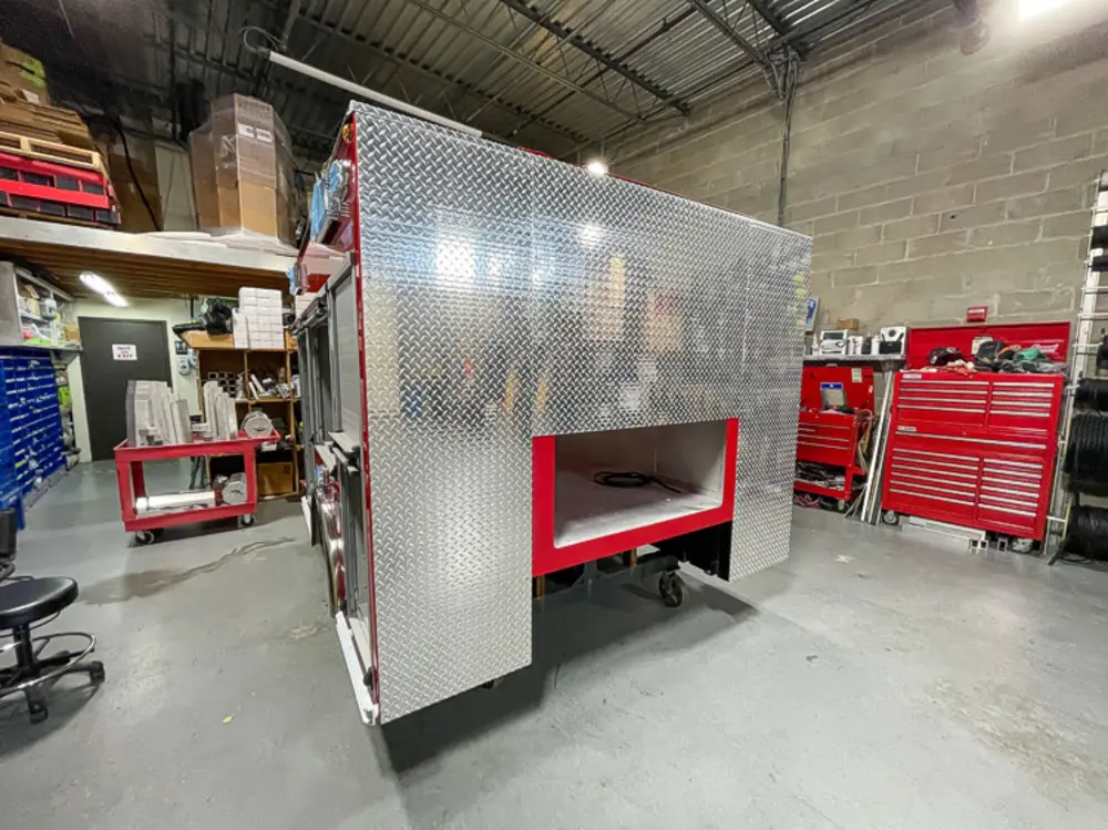 Exterior view of small fire truck showing cab, body compartments, and wheel/tire area.